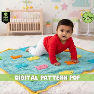 May include: A baby crawls on a turquoise crochet blanket adorned with colorful fish appliqués. The blanket has a yellow and blue border. The words "DIGITAL PATTERN PDF" are displayed on the blanket. The baby wears a red long-sleeved shirt and white pants.