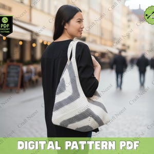 May include: A white and gray crocheted tote bag with a geometric chevron pattern is carried over the shoulder. The bag has a wide strap and is made of a soft, textured yarn. The words "DIGITAL PATTERN PDF" are at the bottom of the image.