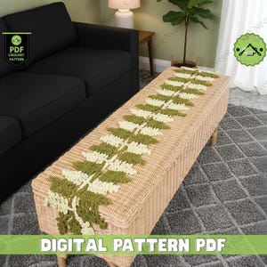Könnte beinhalten: Eine geflochtene Korbbank mit einem gehäkelten Farnblattmuster in Grün und Creme. Die Bank steht vor einem schwarzen Sofa. Der Text "DIGITAL PATTERN PDF" befindet sich am unteren Rand des Bildes.