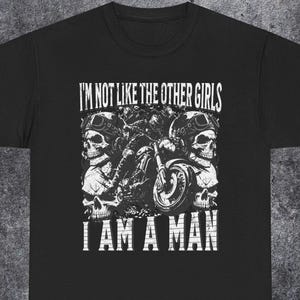Puede incluir: Camiseta negra con un gráfico blanco que presenta una motocicleta, dos calaveras con gafas y el texto "I'M NOT LIKE THE OTHER GIRLS I AM A MAN."
