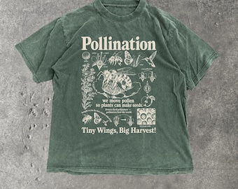 May include: A faded olive green short-sleeve t-shirt featuring a cream-colored graphic print. The design includes illustrations of bees, butterflies, and flowers with the text Pollination, we move pollen so plants can make seeds, and Tiny Wings, Big Harvest!