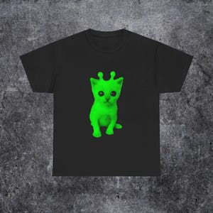 以下が含まれることがあります： 黒いTシャツ。ネオングリーンの子猫のデザインで、エイリアンのような触角が付いています。グラフィックは中央に配置され、明るく珍しい猫を強調しています。Tシャツは柔らかい生地で作られています。