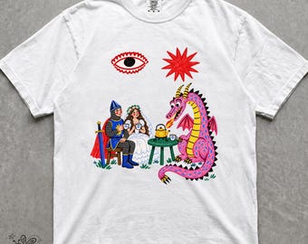 May include: A white short-sleeve t-shirt featuring a graphic print of a knight and a person in a white dress sitting at a small green table with a pink dragon. Above them is a red eye and a red star. The dragon is heating a yellow teapot.