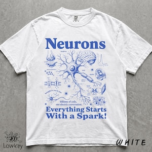 Könnte beinhalten: Ein weißes kurzärmeliges T-Shirt mit einem blauen Grafikdruck eines Neuronendiagramms mit wissenschaftlichen Beschriftungen, einschließlich des Textes "Neurons" oben und "Everything Starts With a Spark!" sowie "billions of cells, one electric conversation." unten.