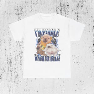 Pode incluir: Camiseta branca com um design gráfico. O design apresenta o texto "I'M PIBBLE WASH MY BELLY" e imagens de um filhote marrom claro, um gato branco e um filhote marrom claro.