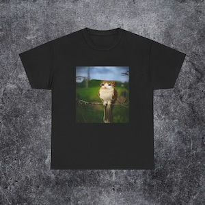 Op de afbeelding: Zwart T-shirt met een vierkante afbeelding van een kat-uil die op een tak zit. De kat heeft bruine en witte vacht, tegen een groene en blauwe achtergrond. Het T-shirt is gemaakt van een zacht, comfortabel materiaal.