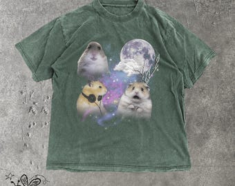 May include: A faded dark green short-sleeve t-shirt featuring a graphic print of three hamsters against a cosmic background with a full moon, purple nebula clouds, and stars. One hamster wears black headphones, while another appears surprised.