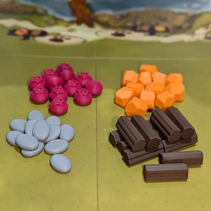 Può includere: Una selezione di pezzi di gioco di varie forme e colori. Ci sono pezzi rosa a forma di bacca, forme geometriche arancioni, gettoni ovali grigi e pezzi a forma di tronco marroni. I pezzi sono disposti su un tabellone verde e giallo.