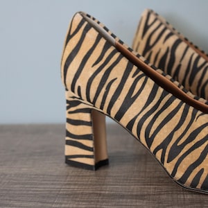 Könnte beinhalten: Ein Paar Pumps mit hohen Absätzen und Zebra-Muster. Die Absätze sind Blockabsätze und die Schuhe sind aus Wildleder.