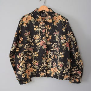 May include: A black button-up jacket with a floral pattern. The jacket has a collared neckline and long sleeves.