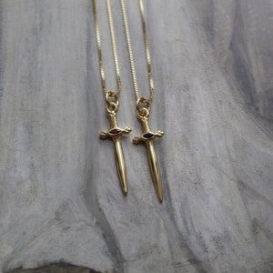 May include: Two gold necklaces with sword pendants. The swords have red and blue gemstones in the center.