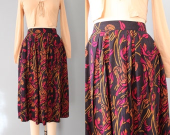 May include: A vintage midi skirt with a black background and a colourful floral pattern in shades of red, pink, and gold. The skirt is paired with a beige long-sleeved top. The skirt is pleated and has a high waist.