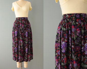 May include: A black midi skirt with a floral print in shades of purple, red, and green. The skirt has a high waist and a pleated design.