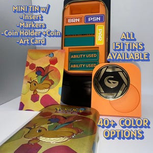 Könnte beinhalten: Ein Pokemon Sammelkartenspiel Mini-Dosen-Set mit einem orangefarbenen Kunststoffeinsatz, Statusmarkern mit der Aufschrift BRN, PSN und PAR, zwei Ability Used Markern, einer schwarz-goldenen Münze, einem Münzhalter und einer illustrierten Karte.