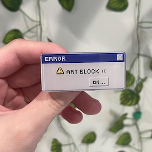 Könnte beinhalten: Ein rechteckiger Anstecker mit einem pixeligen Design, das einer Fehlermeldung ähnelt. Die blaue Kopfzeile lautet "ERROR", und die Nachricht darunter lautet "ART BLOCK :(" mit einem Ausrufezeichen und einem traurigen Gesicht. Der Anstecker hat auch eine "OK..."-Taste.