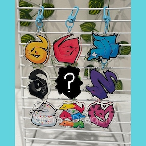 May include: A collection of colorful acrylic keychains featuring cartoon worm designs. The keychains have blue clasps and include various colors such as yellow, red, blue, black, purple, and pink. Some designs have a question mark.