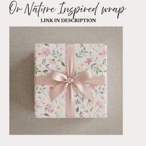 May include: A wrapped gift with floral patterned paper and a blush pink ribbon tied in a bow. The paper features a watercolor design of pink, yellow, and green flowers and leaves on a cream background. Text at the top reads "Or Nature Inspired wrap" and "LINK IN DESCRIPTION".