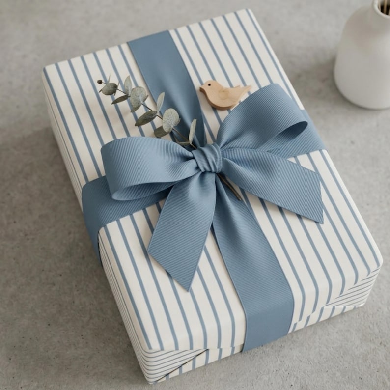 May include: A wrapped gift with blue and white striped paper, tied with a wide blue ribbon and bow. A small wooden bird and sprig of greenery are tucked under the bow, creating a decorative and elegant presentation.