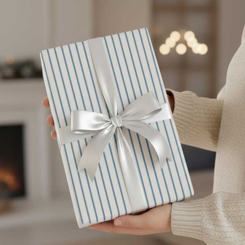 May include: A wrapped gift with blue vertical stripes on white paper, tied with a silver satin ribbon and bow. The gift is held in front of a blurred background.
