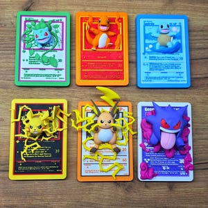 Könnte beinhalten: Sechs farbenfrohe Pokémon-Sammelkarten-Repliken mit Bisasam, Glumanda, Schiggy, Pikachu, Raichu und Gengar. Jede Karte hat eine 3D-Figur des Pokémon und ist vor einem farblich passenden Hintergrund platziert. Die Karten sind auf einer Holzoberfläche angeordnet.