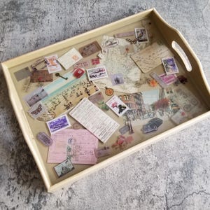 May include: A rectangular wooden serving tray with a clear, glossy surface. The tray is filled with vintage stamps, postcards, and a map. The tray has a light beige frame and integrated handles.