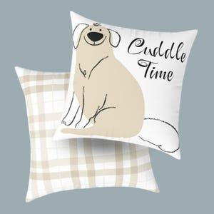 May include: Two decorative throw pillows. One pillow features a beige cartoon dog with the words "Cuddle Time" in black script on a white background. The second pillow has a beige and white plaid pattern.