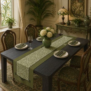 May include: A dark wood dining table set with a sage green damask table runner, white plates, folded green napkins, and wine glasses. A green ceramic vase filled with white hydrangea flowers sits in the center, surrounded by four chairs.