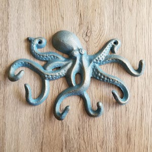 May include: A cast iron octopus wall hook in a distressed blue finish. The octopus has eight curved tentacles that form hooks. The octopus is mounted on a wooden surface.