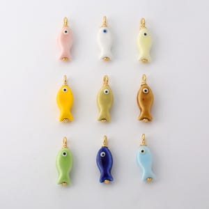 Può includere: Una collezione di nove piccoli ciondoli a forma di pesce in vari colori, tra cui rosa, bianco, giallo, giallo chiaro, verde oliva, marrone, verde lime, blu scuro e azzurro. Ogni ciondolo presenta un dettaglio a occhio e un occhiello dorato.