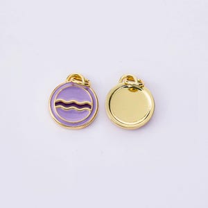 Può includere: Due ciondoli rotondi color oro. Un ciondolo presenta un design in smalto viola con una linea ondulata, l'altro è di colore oro pieno. Entrambi hanno un piccolo anello nella parte superiore per attaccarli a una catena o un braccialetto.