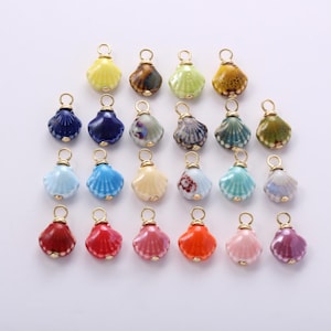 May include: A collection of twenty-three small, ceramic seashell-shaped charms in various colors including yellow, blue, green, red, orange, pink, and purple. Each charm features a gold-toned metal jump ring attached to the top for hanging.