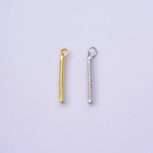 May include: Two pendant charms, one gold-toned and one silver-toned, each with a vertical bar design. The bars are encrusted with small, sparkling stones. Each charm has a small loop at the top for attaching to a chain or bracelet.