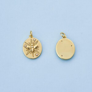 May include: Two gold-colored pendants. One pendant features a bee design with a sunburst pattern and small crystals. The other pendant is a plain gold circle with three small holes. Both pendants have a small loop at the top for attaching to a chain.