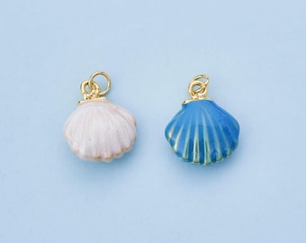 May include: Two seashell charms. One is white with a gold-colored bail, and the other is blue with a gold-colored bail. The charms are on a light blue background. These charms are suitable for jewelry making or other craft projects.