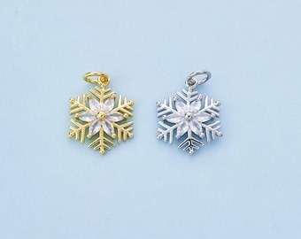 Könnte beinhalten: Zwei Schneeflocken-Anhänger, einer goldfarben und einer silberfarben, jeweils mit einem zentralen Blumenmuster. Die Anhänger befinden sich auf einem hellblauen Hintergrund. Der goldene Anhänger hat eine goldene Schlaufe, und der silberne Anhänger hat eine silberne Schlaufe.