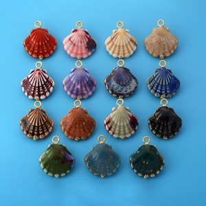 Könnte beinhalten: Eine Sammlung von vierzehn Jakobsmuschel-Anhängern, angeordnet in vier Reihen. Jede Muschel weist ein einzigartiges Farbmuster auf, darunter Rot, Rosa, Beige, Braun, Violett, Blau, Grün und Schwarz, mit einem kleinen goldfarbenen Metallring oben.