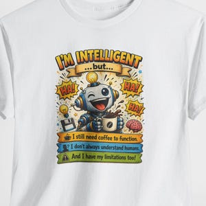 Op de afbeelding: Wit t-shirt met een cartoon robot en de tekst "I'M INTELLIGENT...but..." en de zinnen "I still need coffee to function," "I don't always understand humans," en "And I have my limitations too!"