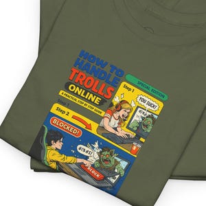 Könnte beinhalten: Zwei olivgrüne T-Shirts sind gefaltet und gestapelt. Das obere Shirt zeigt eine Comic-Grafik mit dem Text "HOW TO HANDLE TROLLS ONLINE" und Illustrationen von Online-Interaktionen. Die Grafik enthält die Wörter "BLOCKED!" und "YOU SUCK!"