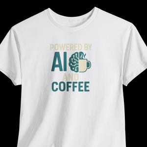 Può includere: T-shirt bianco con la scritta "POWERED BY AI AND COFFEE" in tonalità verde acqua e beige. Il design include un cervello e una tazza di caffè, suggerendo un tema di tecnologia e caffeina.