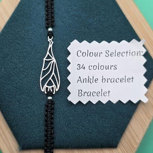 Op de afbeelding: Zwart macramé armband met een zilveren vleermuisvormige hanger. De hanger heeft een gedetailleerd, open ontwerp. Een wit label toont "Colour Selection: 34 colours Ankle bracelet Bracelet."