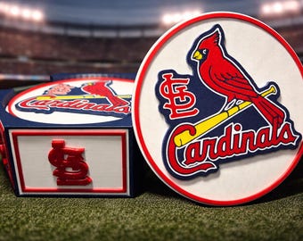 Puede incluir: Un logotipo de los Cardenales de San Luis se muestra en una caja y un emblema redondos blancos, rojos y azules. El logotipo presenta un pájaro cardenal rojo posado en un bate de béisbol amarillo, con el nombre y las iniciales del equipo.
