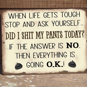 May include: A white sign with black text that reads "When life gets tough stop and ask yourself... Did I shit my pants today? If the answer is no. Then everything is going O.K.!". The sign has two black poop emojis on either side of the text.