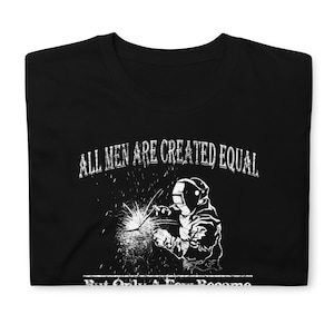 May include: Black t-shirt with a white graphic design. The graphic features a welder with a welding torch and the text "All men are created equal, but only a few become welders."