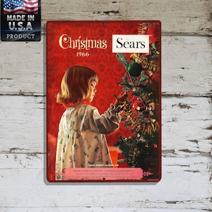 May include: Vintage Christmas-themed metal sign featuring a young girl decorating a Christmas tree. The sign has a red background with the words "Christmas 1966" and "Sears" printed on it. The sign also has a "Made in U.S.A. Product" label.
