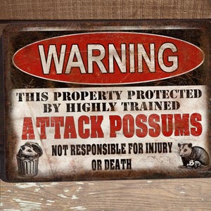 May include: A rusty metal sign with a red circle and the word "WARNING" in white. The sign reads "This property protected by highly trained attack possums. Not responsible for injury or death."