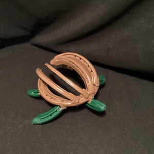 May include: A brown horseshoe turtle sculpture with green painted legs. The turtle is made from two horseshoes that are bent and welded together to form the shell.