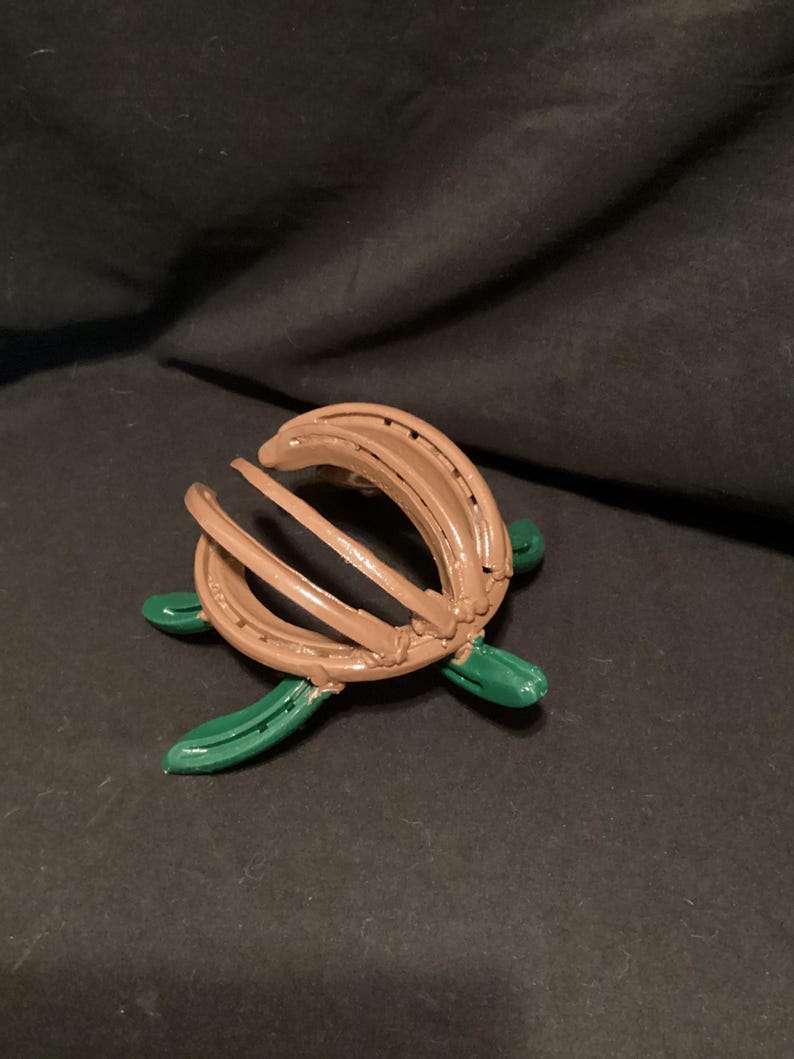May include: A brown horseshoe turtle sculpture with green painted legs. The turtle is made from two horseshoes that are bent and welded together to form the shell.