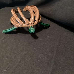 May include: A brown horseshoe sculpture with green accents. The sculpture is made of multiple horseshoes that are bent and welded together to form a unique design.