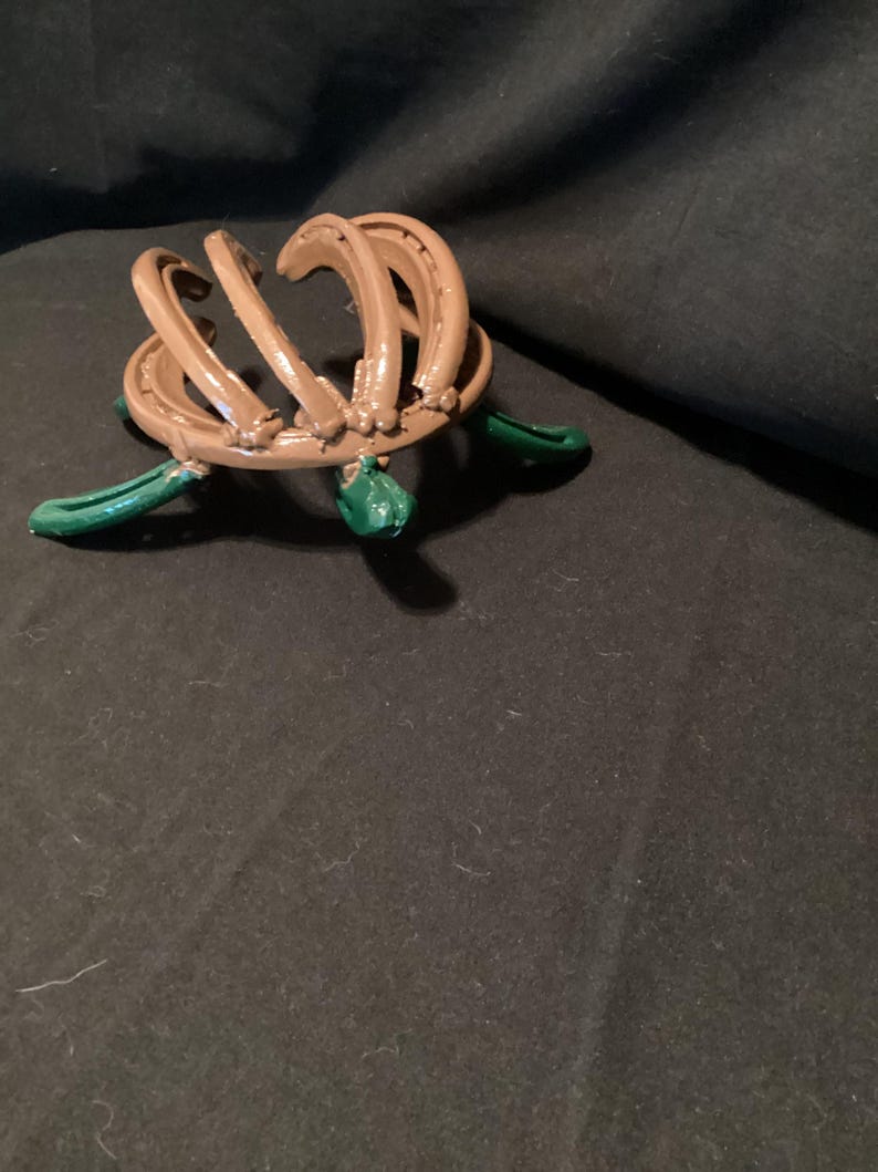 May include: A brown horseshoe sculpture with green accents. The sculpture is made of multiple horseshoes that are bent and welded together to form a unique design.