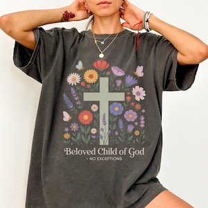 May include: Dark gray t-shirt featuring a floral cross design with butterflies and the text "Beloved Child of God - NO EXCEPTIONS". The design includes colorful flowers in shades of red, yellow, purple, and blue.